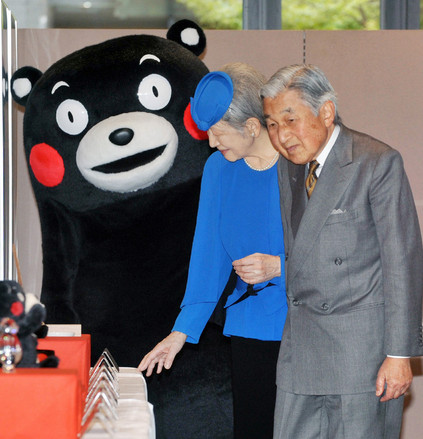 2013年10月28日，明仁天皇和美智子在参观日本南部的熊本县(Kumamoto)时，站在黑色萌熊吉祥物“熊本熊”(Kumamon)旁边。